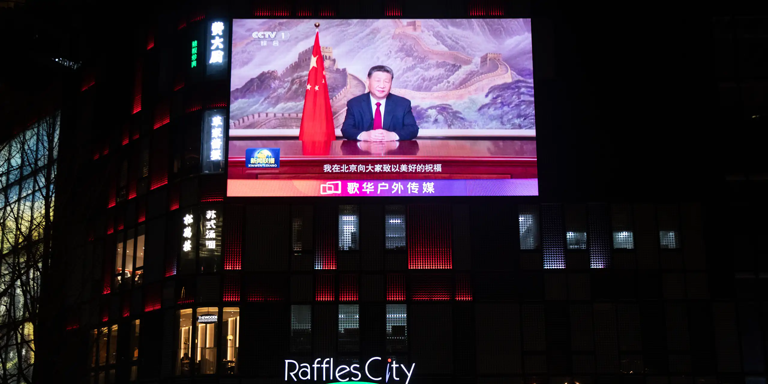 People walk past a screen showing Xi's televised address.
