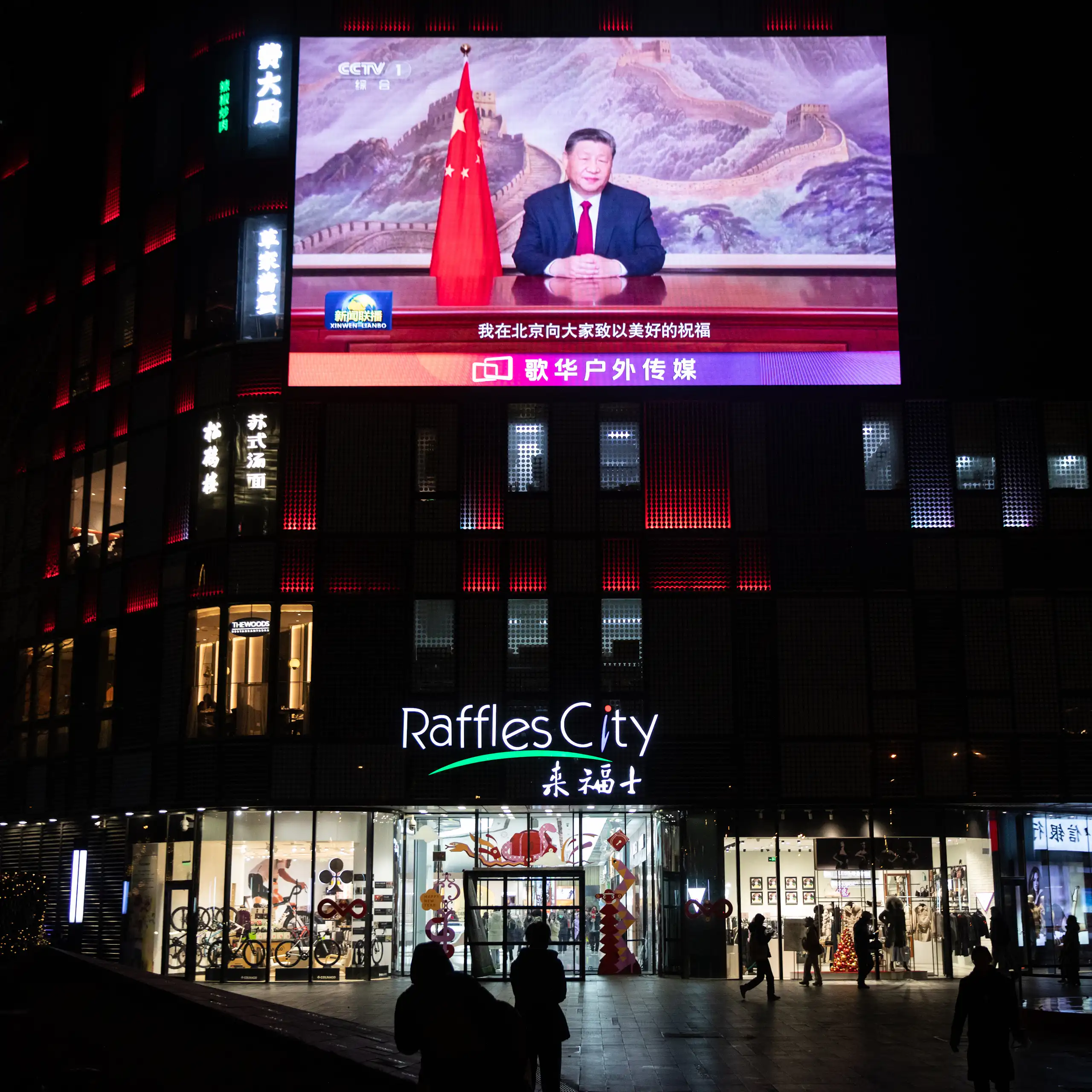 People walk past a screen showing Xi's televised address.