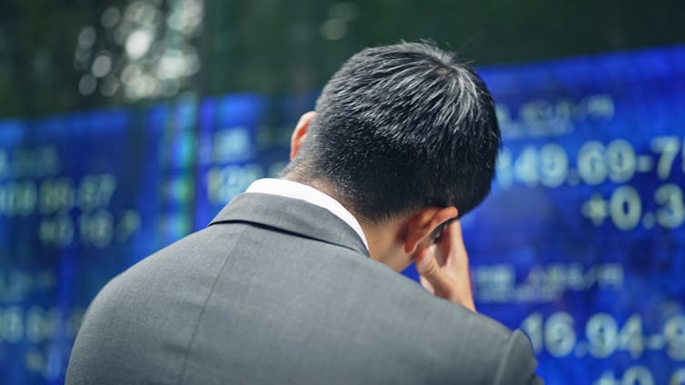 A businessman with his head in his hands as he looks at an electric bulletin board.