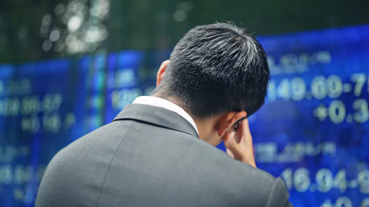 A businessman with his head in his hands as he looks at an electric bulletin board.