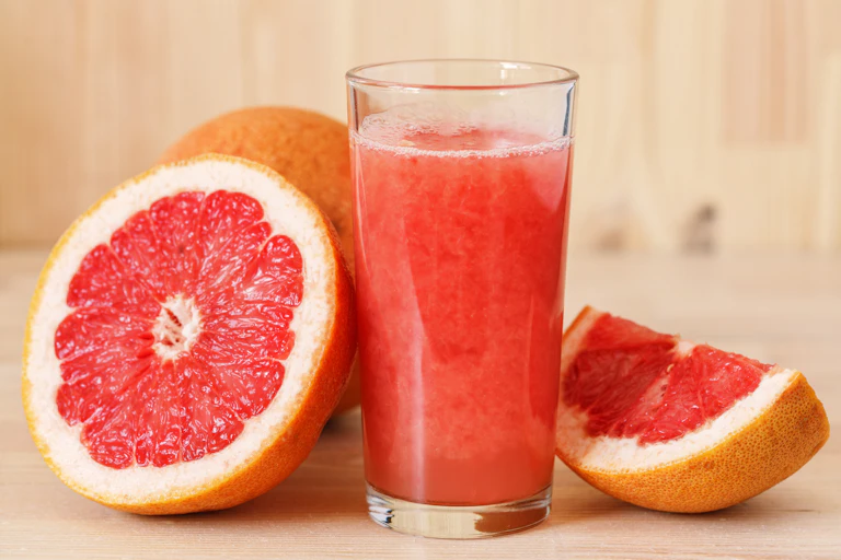 A glass of freshly squeeze grapefruit juice, with grapefruit slices sitting beside it.