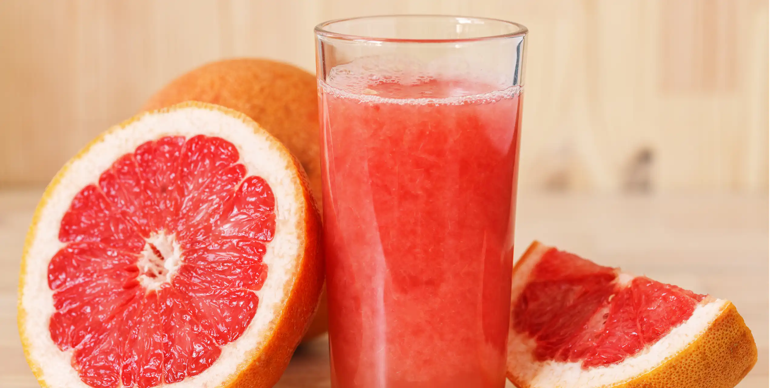 A glass of freshly squeeze grapefruit juice, with grapefruit slices sitting beside it.