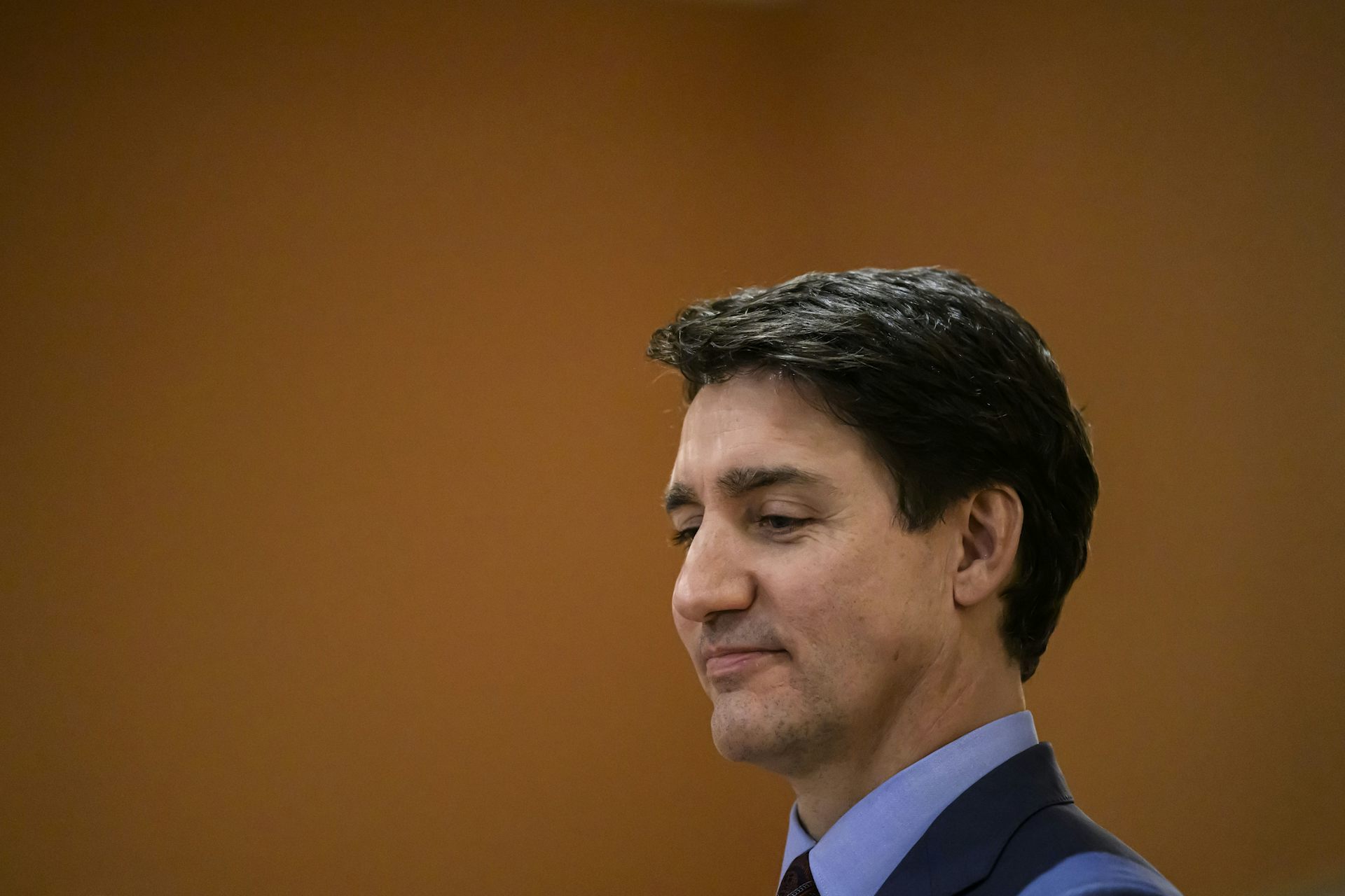 Un homme brun regarde vers le bas avec un léger sourire sur le visage