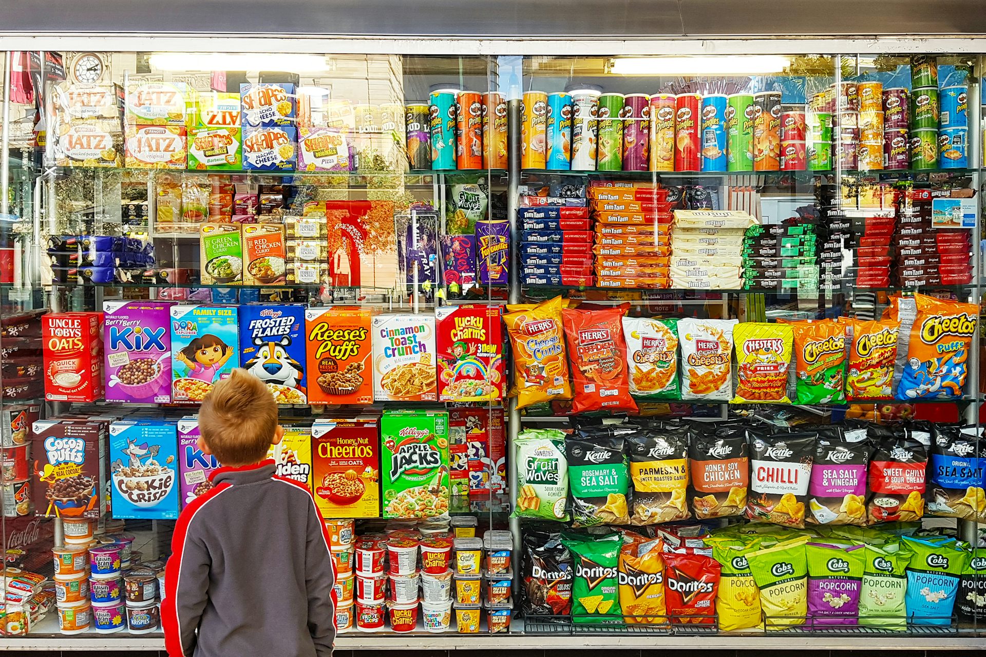 un enfant devant un rayon de chips, céréales petit-déjeuner et autres aliments ultratransformés