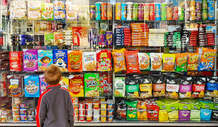 un enfant devant un rayon de chips, céréales petit-déjeuner et autres aliments ultratransformés