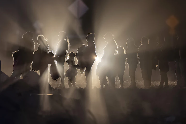Immigrants, illuminated by car lights, form a line on the U.S.-Mexico border.