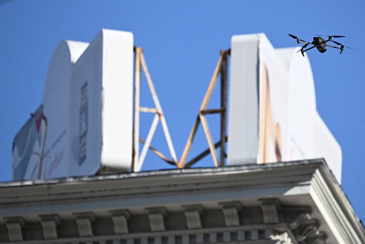 Drone pictured flying in air near top of nearby building with blue sky in background