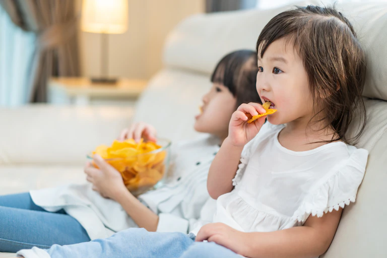 Deux petites filles mangent des chips assises sur un sofa