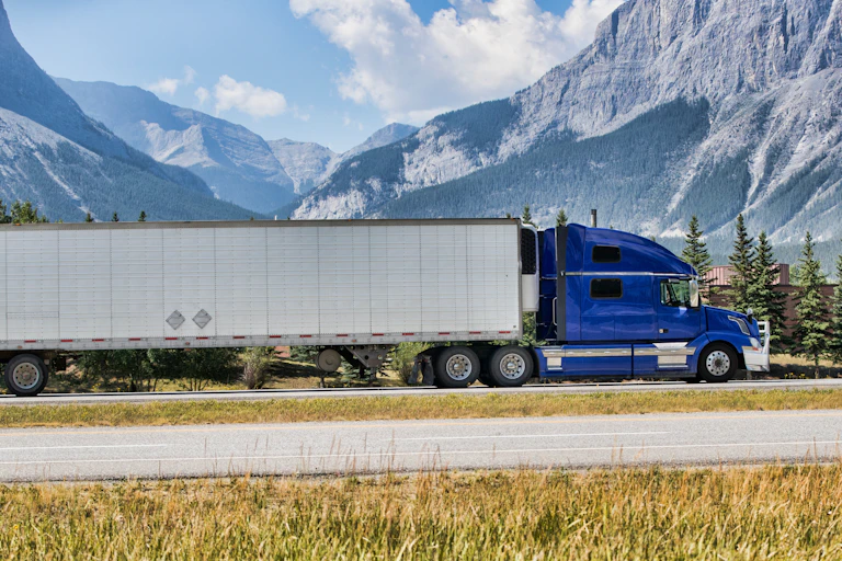 A transport truck with a bright-blue cab travels along a mountainous highway.