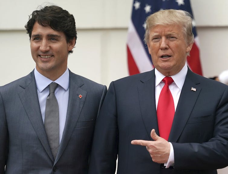 Two men in suits stand next to each other, one pointing at the other