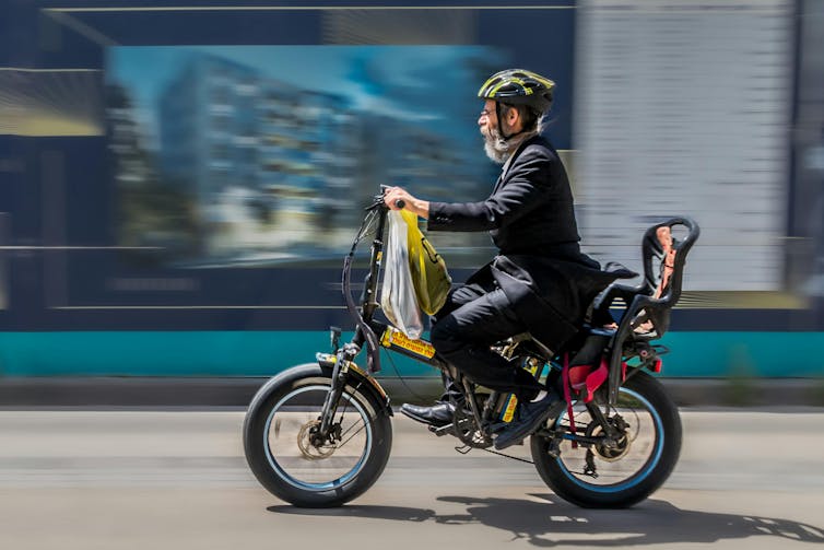 A man with a white beard speeds on an electric bike in the city.