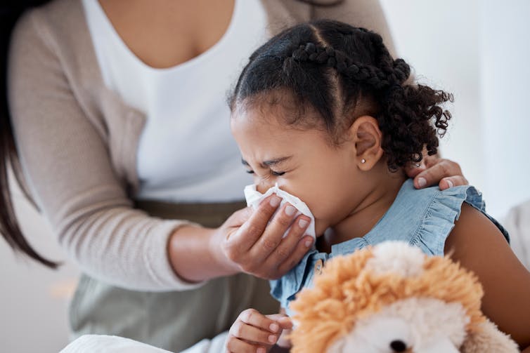 An adult helps a young girl to blow her nose.