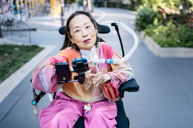 A woman in brightly coloured clothes, in a wheelchair, looks at the camera
