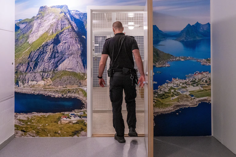 A prison officer walks through a doorway in Norway's Ringerike prison, with a photograph mural of a beautiful nature scene surruonding the doorway