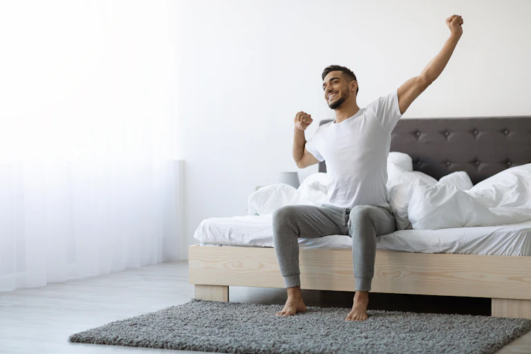 A man sitting in bed stretches after a good night's sleep.