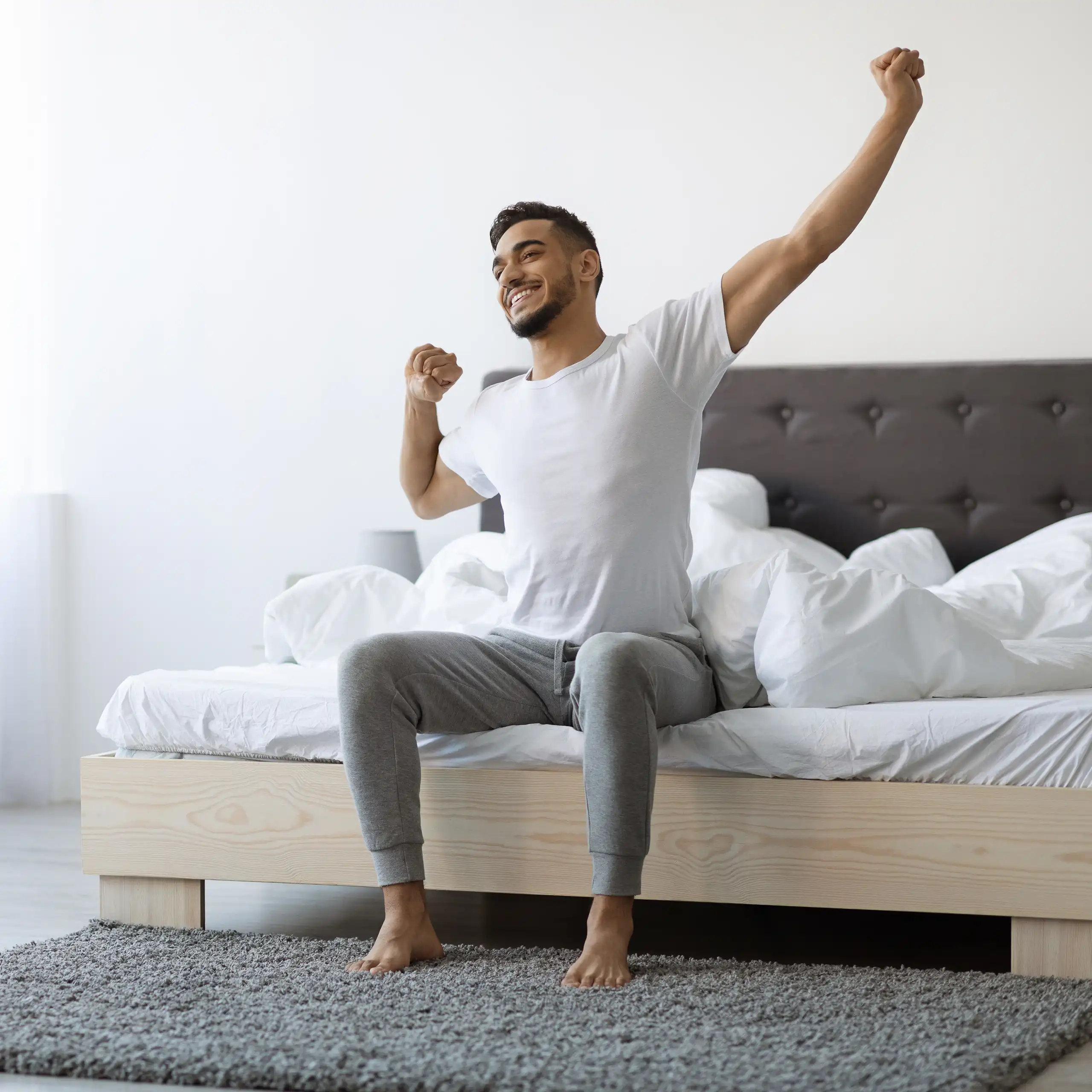 A man sitting in bed stretches after a good night's sleep.