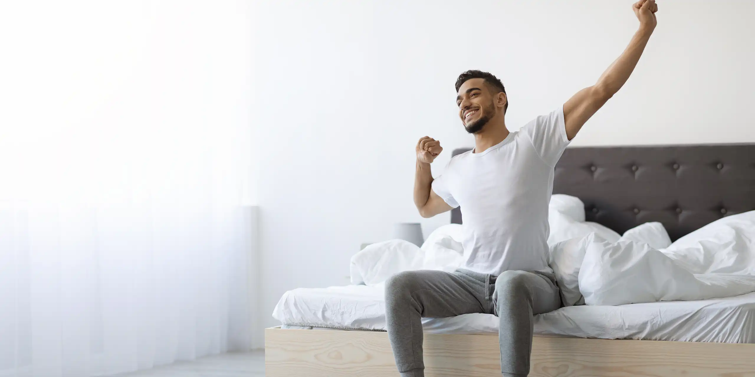 A man sitting in bed stretches after a good night's sleep.