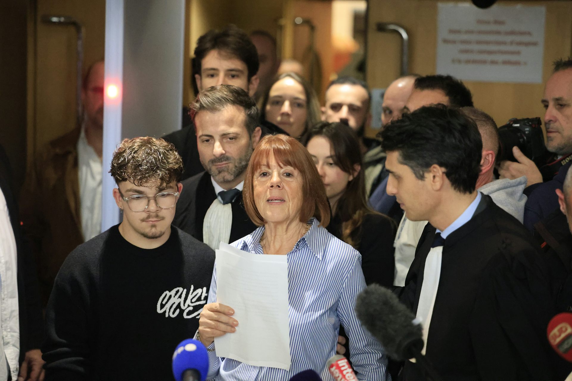 Gisele Pelicot speaking into microphones with a crowd of supporters behind her.