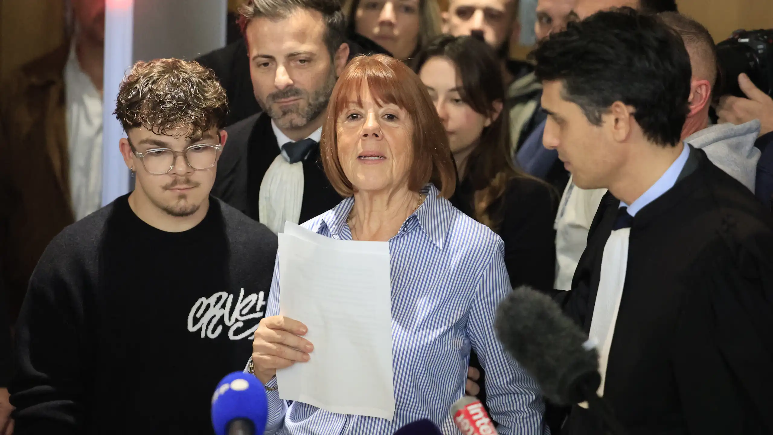 Gisele Pelicot speaking into microphones with a crowd of supporters behind her.