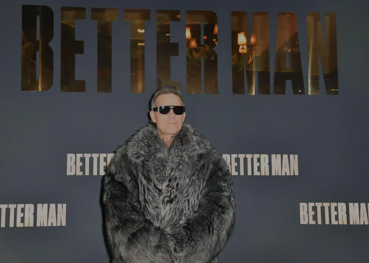 A man with grey cropped hair, wearing sunglasses and a fur coat at a film premiere