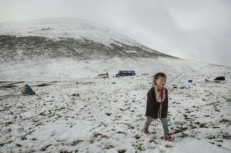 small child in largely empty landscape that's dusted with snow