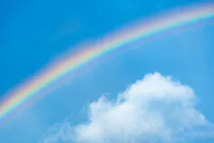A rainbow stretches across a blue sky with some clouds.