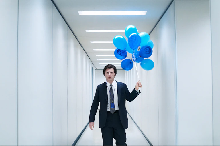 Adam Scott in a white hallway holding blue balloons