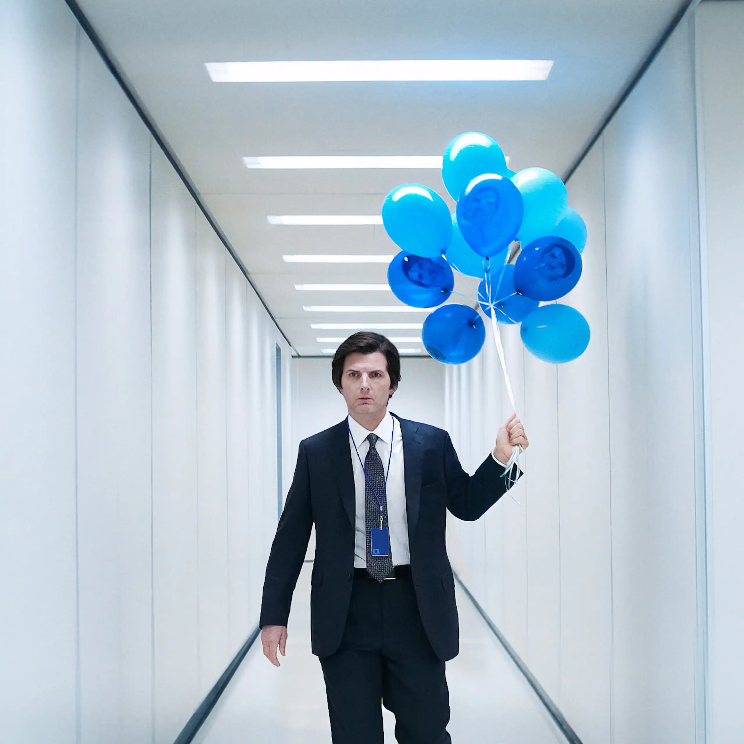 Adam Scott in a white hallway holding blue balloons