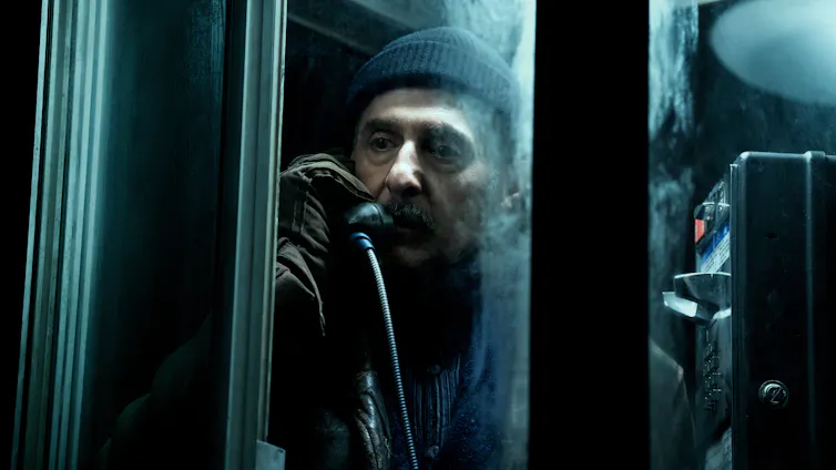 An elderly man in a dark phone booth