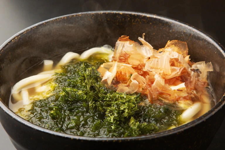 un bol contenant une bouillon avec des nouiles et des algues vertes.