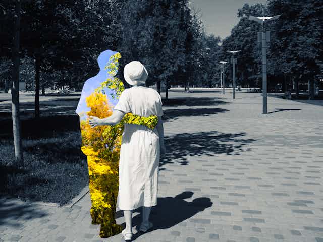 a couple from the back walking in a park, the woman and background in black and white, the man a silhouette enclsoing a color view of trees and sky