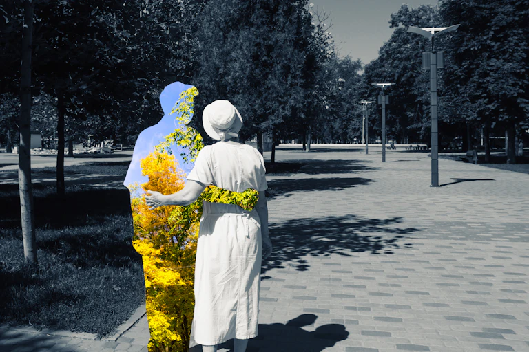 a couple from the back walking in a park, the woman and background in black and white, the man a silhouette enclsoing a color view of trees and sky