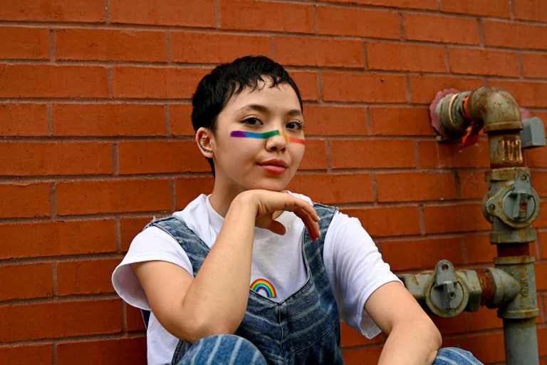 A young Asian person with the rainbow flag on their face.