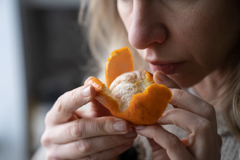 A woman holds a half-peeled mandarin to her nose.