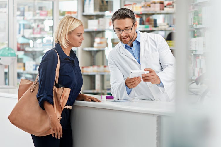 A woman speaks over the counter to a male pharmacist.