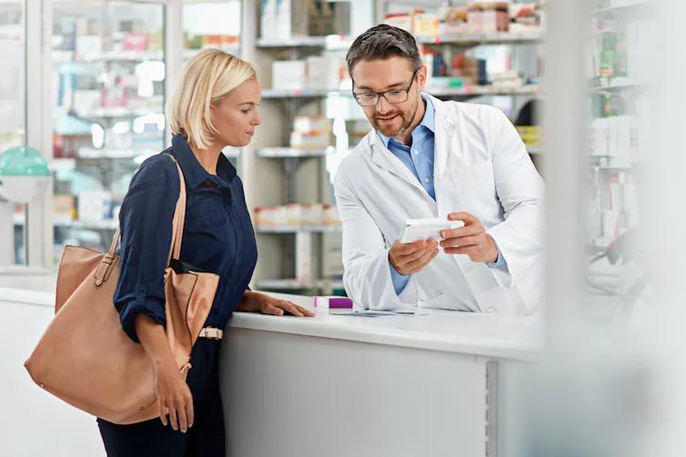A woman speaks over the counter to a male pharmacist.
