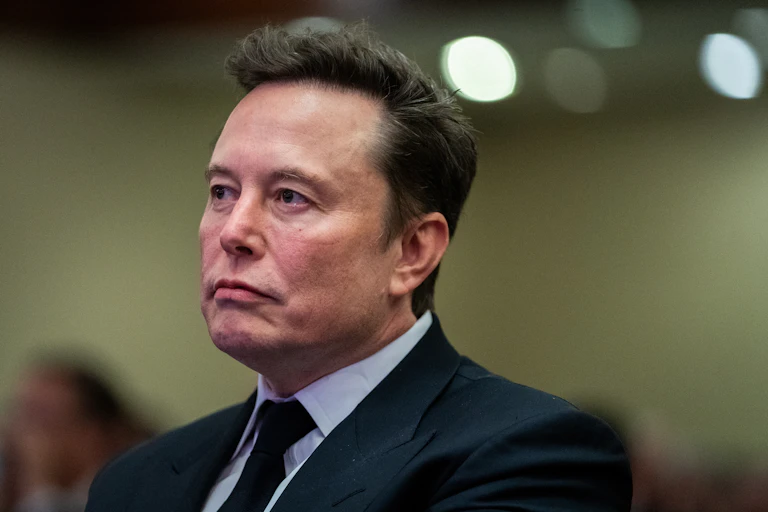 Elon Musk wearing a suit and a frown