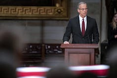A man in a suit and tie speaks from a lectern.