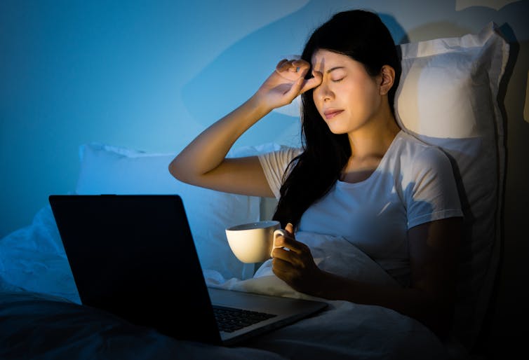 stressed woman in bed looking at a laptop