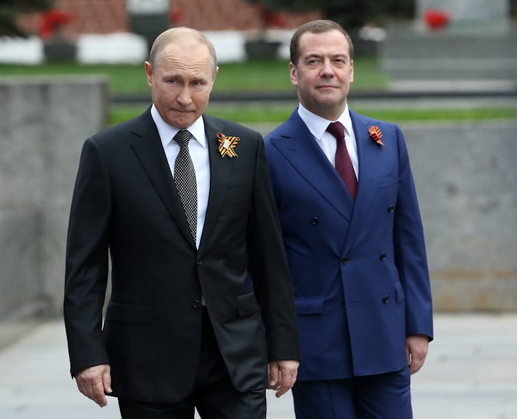 Two men in suits stand in an open area.