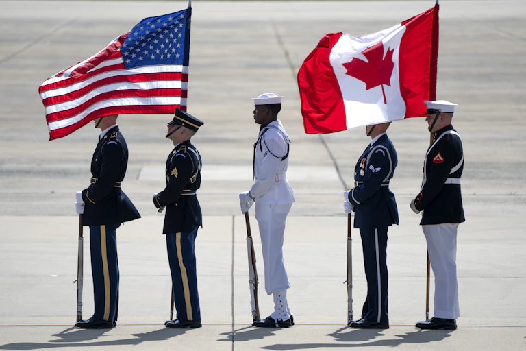 Honour guards stand on an airport tarmac holding an American and Canadian flag.
