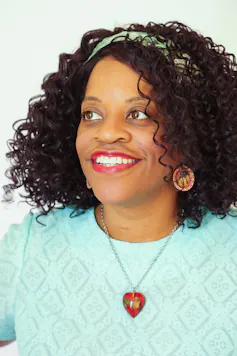 A smiling Black woman with a heart-shaped necklace and a headband.