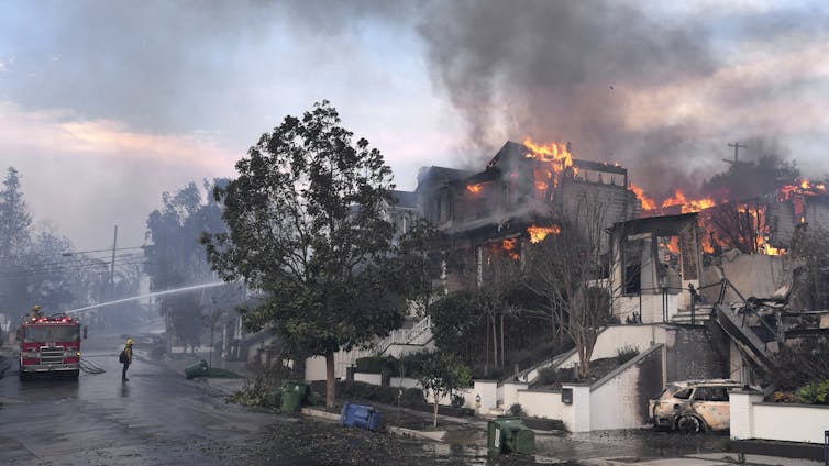 A fire truck sprays water from the street as homes burn on a hillside.