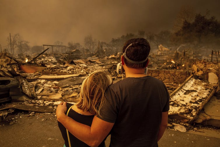 A couple stare at a fire damaged home