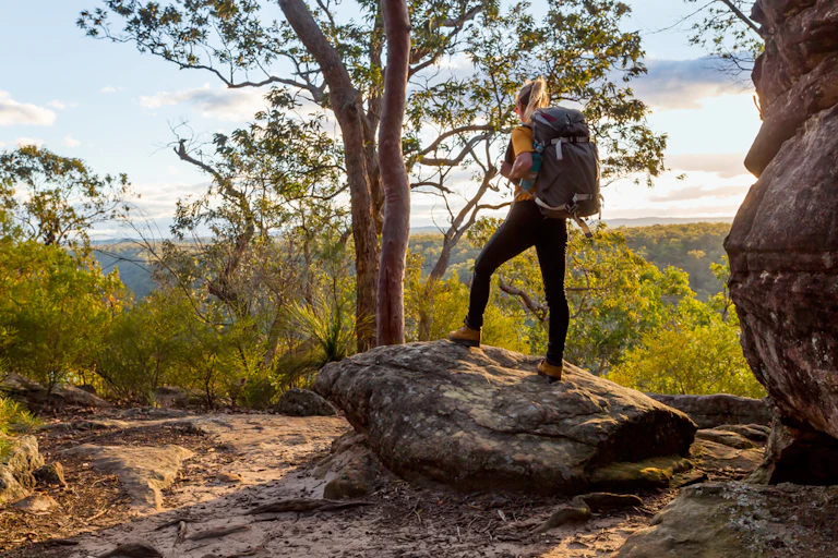 Female bushwalker with backpack on rock looking out at Australian