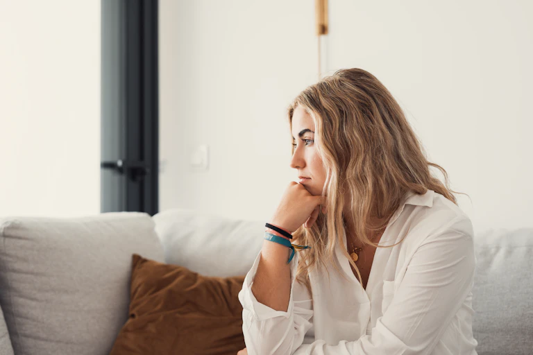 A woman sitting along on a couch with a contemplative expression.
