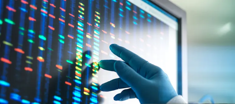 Gloved handed researcher touching screen of DNA sequences in bright colours