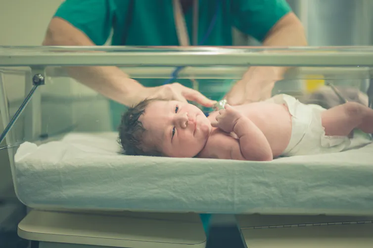 Health worker examining newborn baby in hospital bassinet