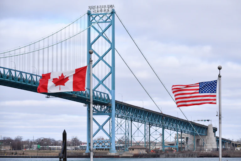 A Canadian flag and an American flag stand in front of a suspension bridge