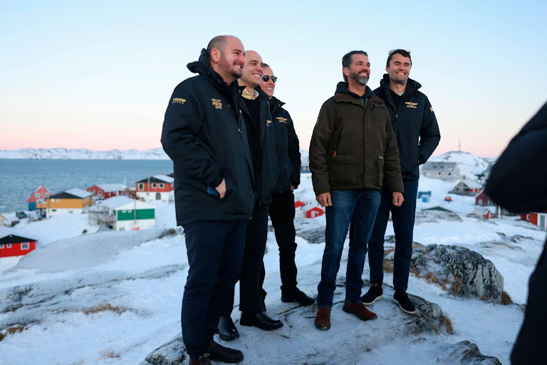 Donald Trump Junior stands on a snowy ridge with men in jackets in Greenland.